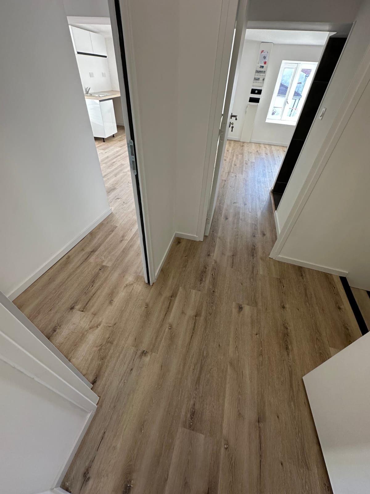 Couloir avec sol en PVC imitation bois et murs blancs, finition mat