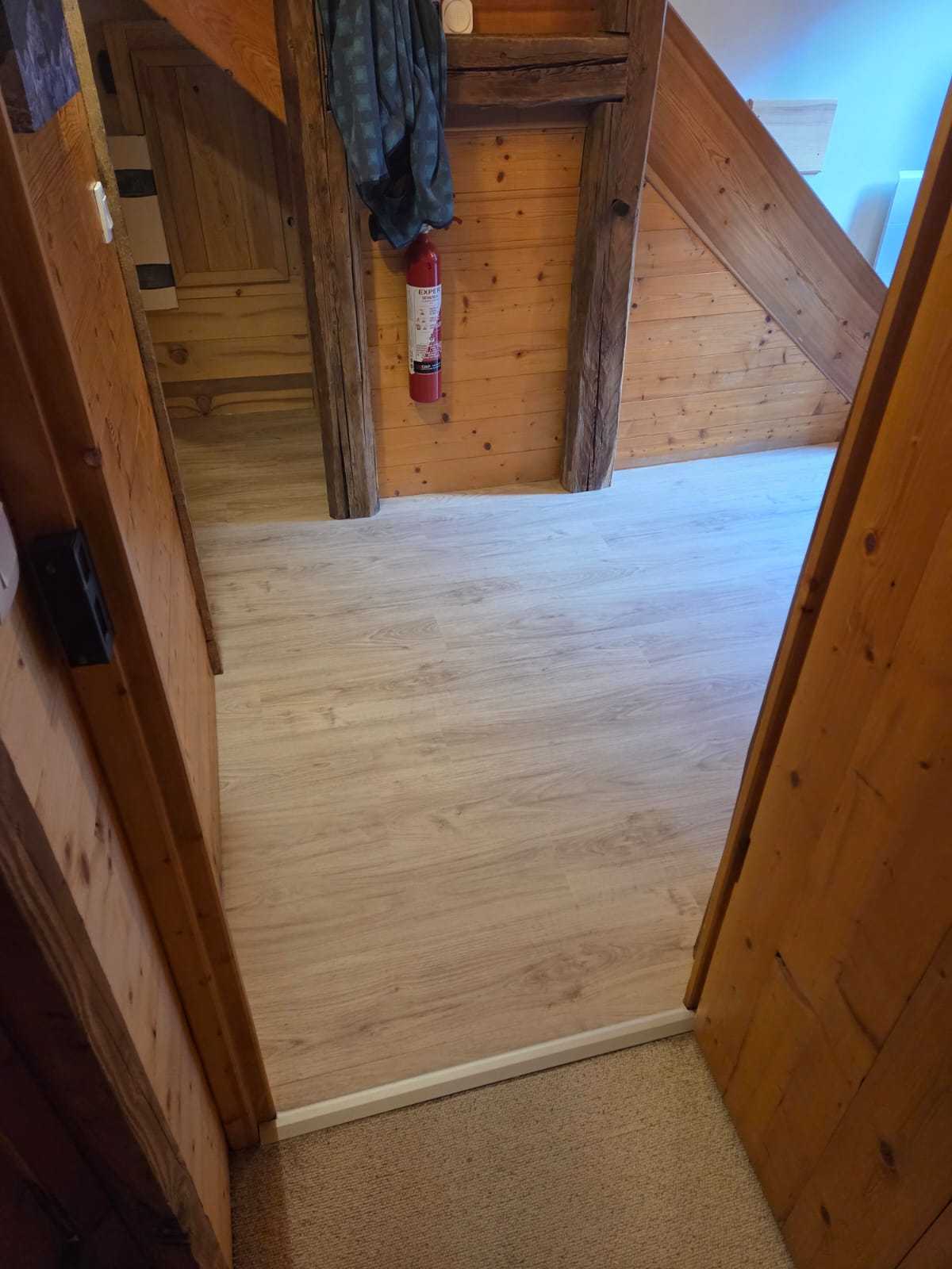 Couloir avec sol en PVC blanc et murs en bois clair, finition mat.